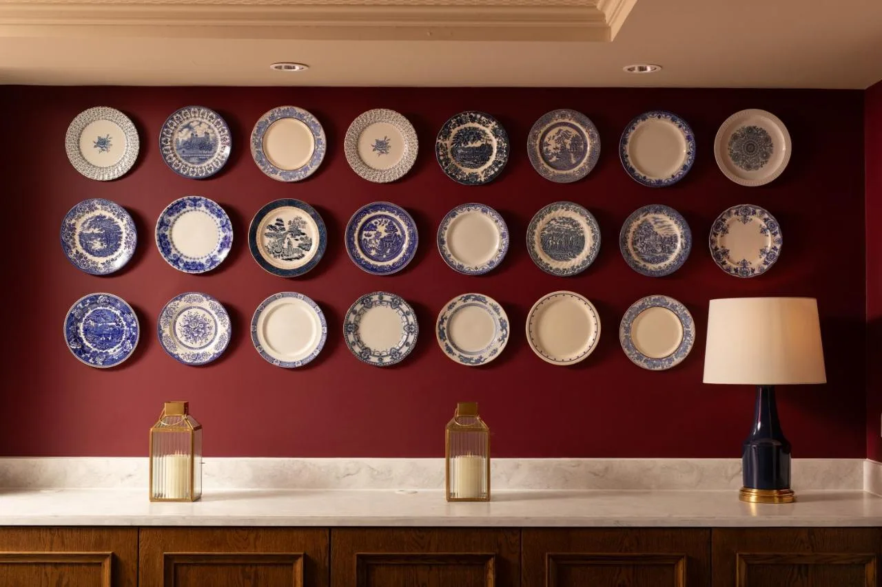a wall of plates on a red wall with a lamp at The Scholar in Edinburgh